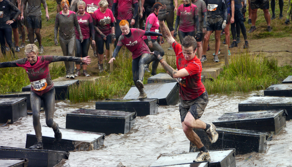 People crossing water on platforms as part of a Tough Mudder
work team challenge for charity