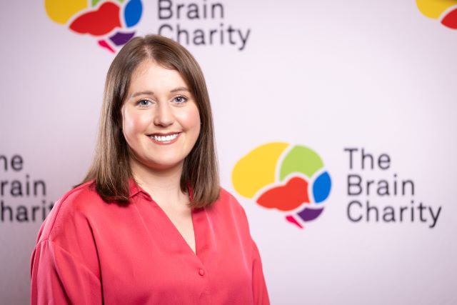 Headshot of Tui Benjamin Thorp smiling at the camera against a background with Brain Charity logos
